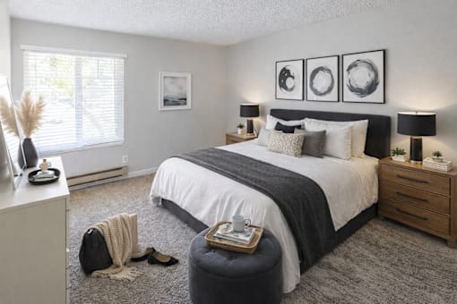 A bedroom with a large bed, a nightstand, and a window with blinds.