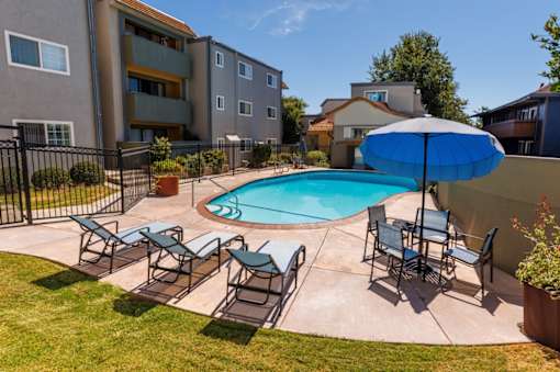 A pool surrounded by chairs and an umbrella in a backyard.