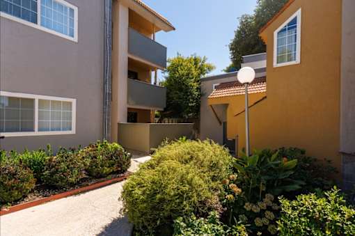 A building with a balcony and a bushy garden in front.
