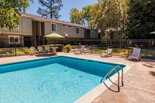 A swimming pool in a backyard with a fence and chairs.
