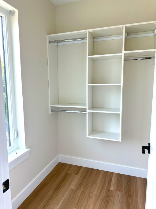 a walk in closet with white shelving and a window