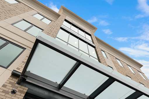 A building with a mix of brick and panel construction features large windows and a balcony with glass railings.