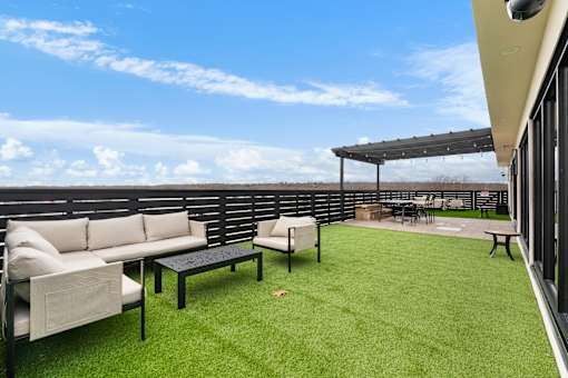 A patio with a white couch, black table, and a green lawn.
