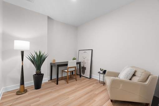 A den office with a couch, a desk, a chair, a lamp, and a plant.