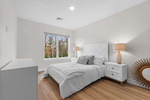 A bedroom with a large bed, a nightstand, and a window with a view of trees.