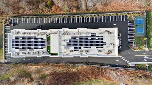 A parking lot with a building and solar panels on the roof.