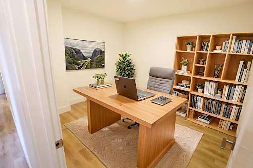 A room with a desk, a laptop, a phone, a potted plant, and a bookshelf.