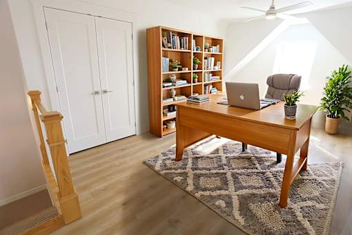A room with a wooden desk, a laptop, a bookshelf, and a potted plant.