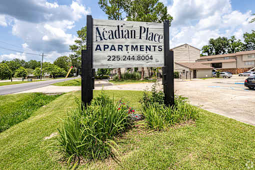 A sign for Acadian Place Apartments stands in front of a building.