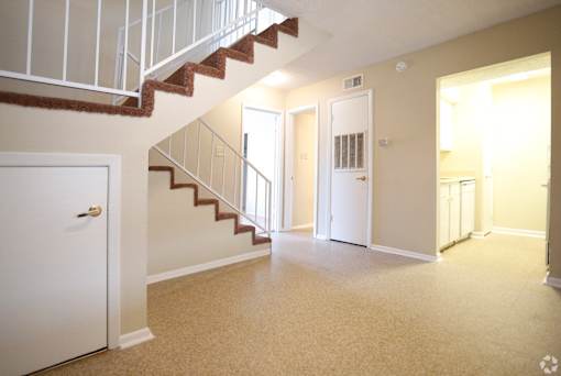 A white door is on the left of a hallway with a staircase.