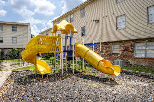 A yellow slide in a playground with a building in the background.