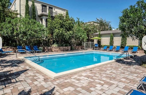 A swimming pool surrounded by blue lounge chairs and trees.