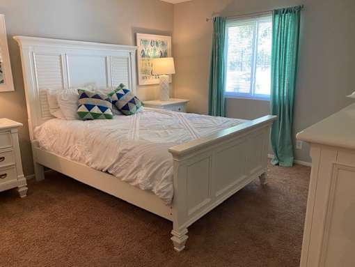 A white bed with a white headboard and a white nightstand with a lamp on it.