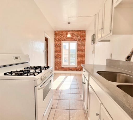 A kitchen with a white stove, white cabinets, and a brick wall.