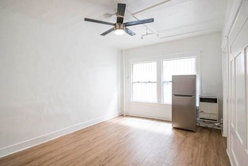 A room with a ceiling fan and a refrigerator.