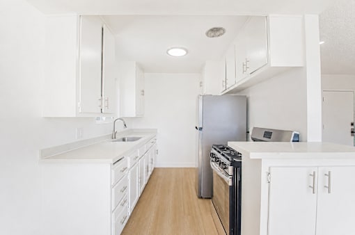 A white kitchen with a stove, sink, and refrigerator.