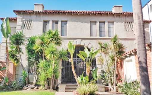 A house with a black gate and a white door surrounded by green plants.