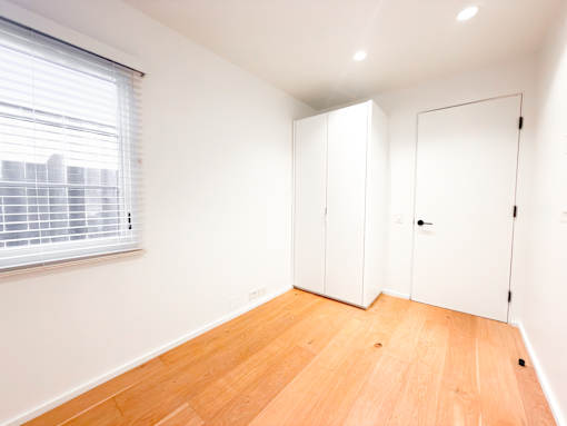 A room with white walls, wooden floors, and a window with blinds.
