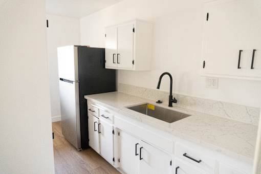 A black refrigerator sits next to a sink in a kitchen with white cabinets.