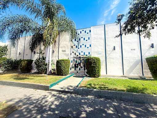 A white building with a blue pattern on the side and a green pathway leading to the entrance.