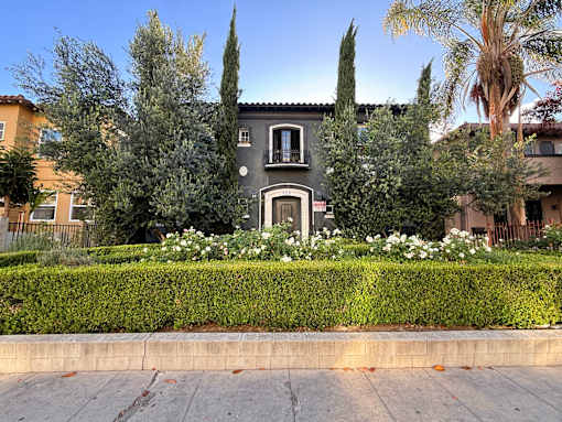 A house with a grey facade is surrounded by greenery and white flowers.