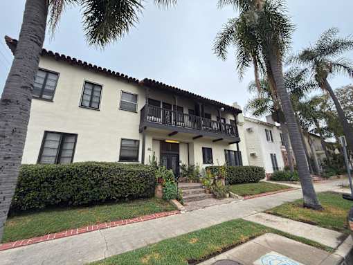 A white house with a balcony and a red brick walkway.