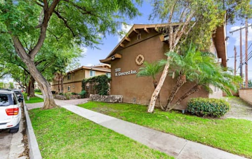 the sidewalk in front of an apartment building with trees and grass