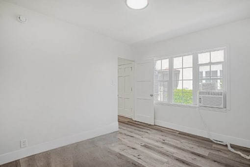 A room with a white door, a window with a white frame, and a light on the ceiling.