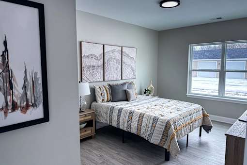 A bedroom with a bed, nightstand, and a painting on the wall.