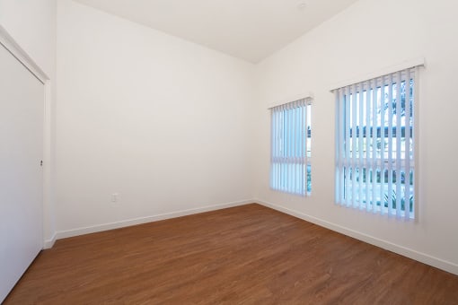 an empty room with wood flooring and two windows