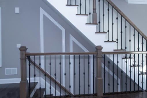 the bottom of a staircase with a wooden railing and a white wall