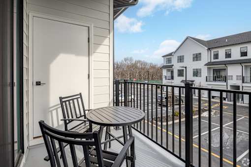 A balcony with a table and chairs overlooks a parking lot.