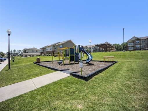 a playground with a blue slide in front of some apartments at The Maddox Apartments, Centerton, Arkansas