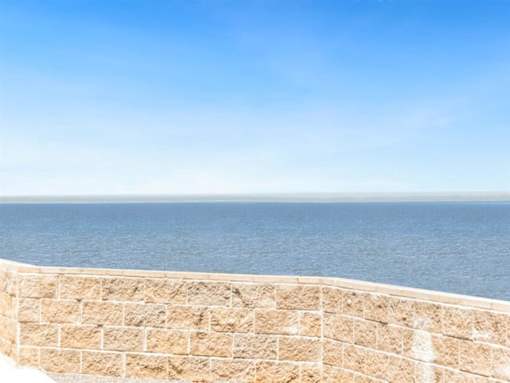 a view of the ocean from a balcony with a stone wall