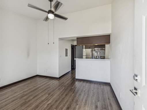 an empty living room with a kitchen and a ceiling fan