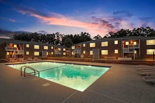 an apartment pool with a sunset in the background at dusk