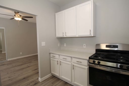 a kitchen with white cabinets and a stove and a ceiling fan