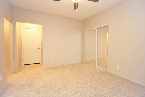 an empty bedroom with mirrored closet doors and a ceiling fan