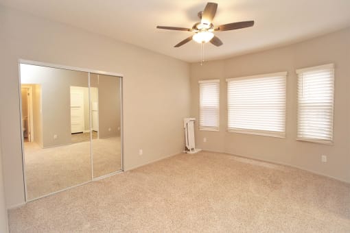 an empty bedroom with a ceiling fan and a mirror
