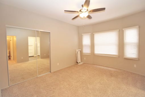 an empty bedroom with a ceiling fan and a mirror