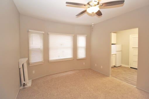 an empty living room with a ceiling fan and three windows