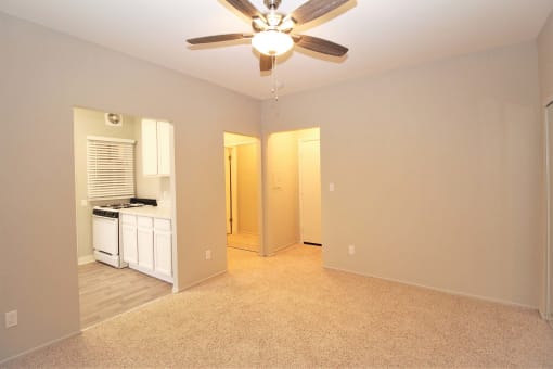 an empty living room with a ceiling fan and a kitchen