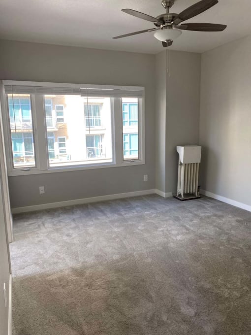 an empty living room with a ceiling fan and three windows