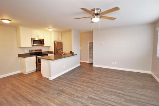 an empty living room with a kitchen and a ceiling fan