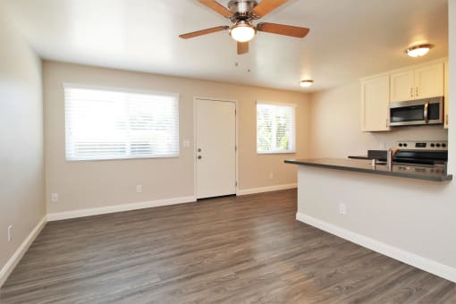 an empty living room with a kitchen and a ceiling fan