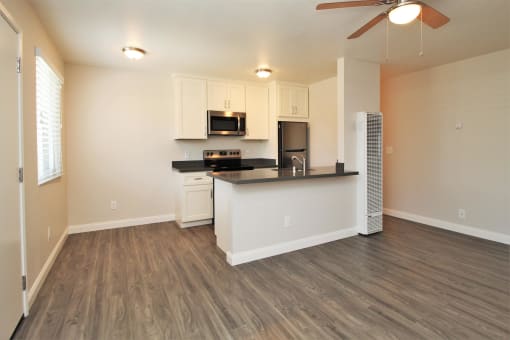 an empty living room with a kitchen and a ceiling fan