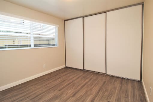 a bedroom with white walls and wood flooring and a window