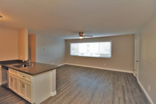 an empty living room with a kitchen and a ceiling fan