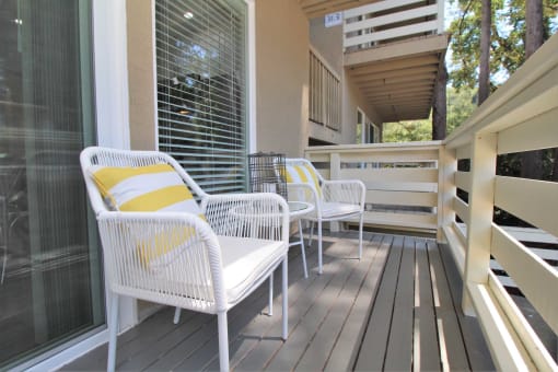 a porch with white wicker chairs and a yellow and white pillow