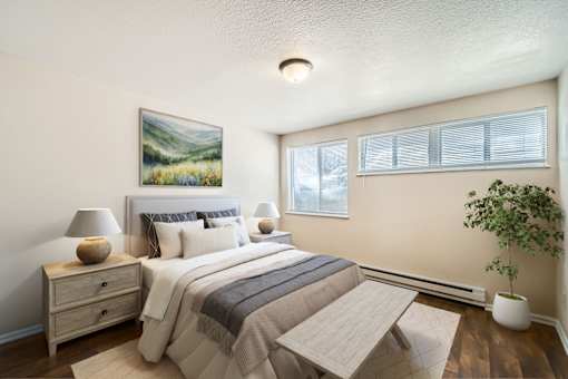 A bedroom with a large bed, a nightstand with a lamp, a painting on the wall, and a potted plant.